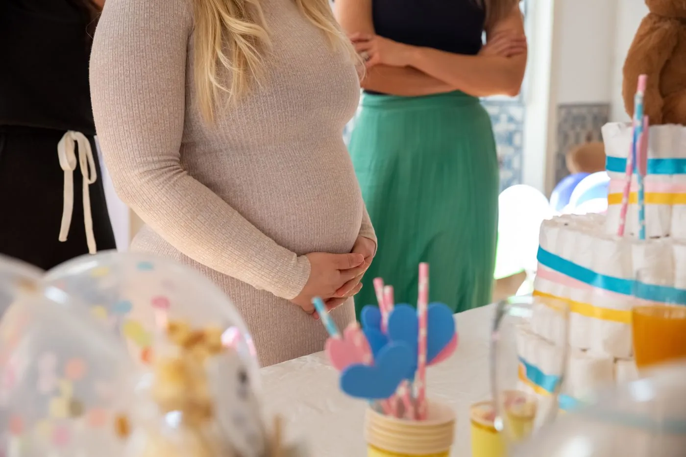 Detail těhotenského bříška s balónky a dortem v pozadí
