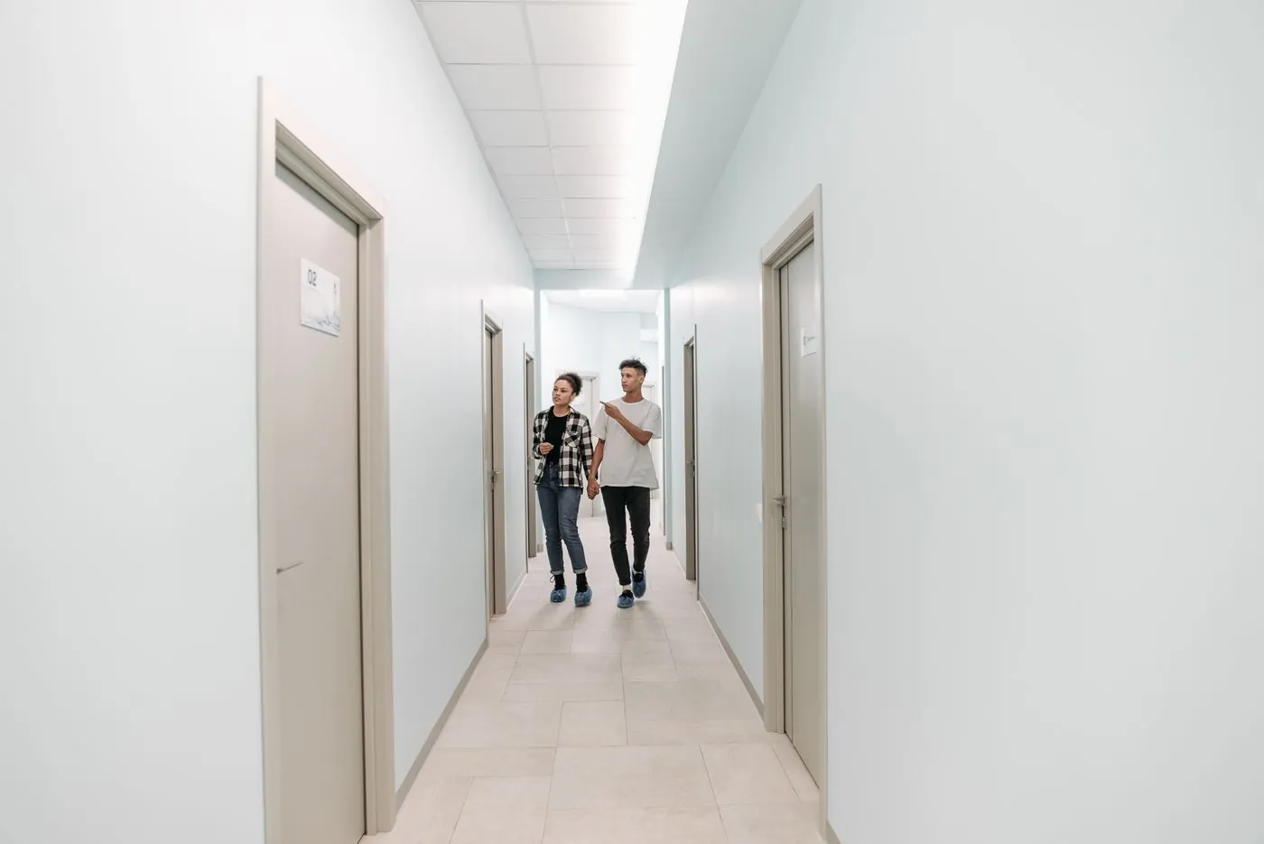 Pár prochází světlou chodbou moderní porodnice s více dveřmi