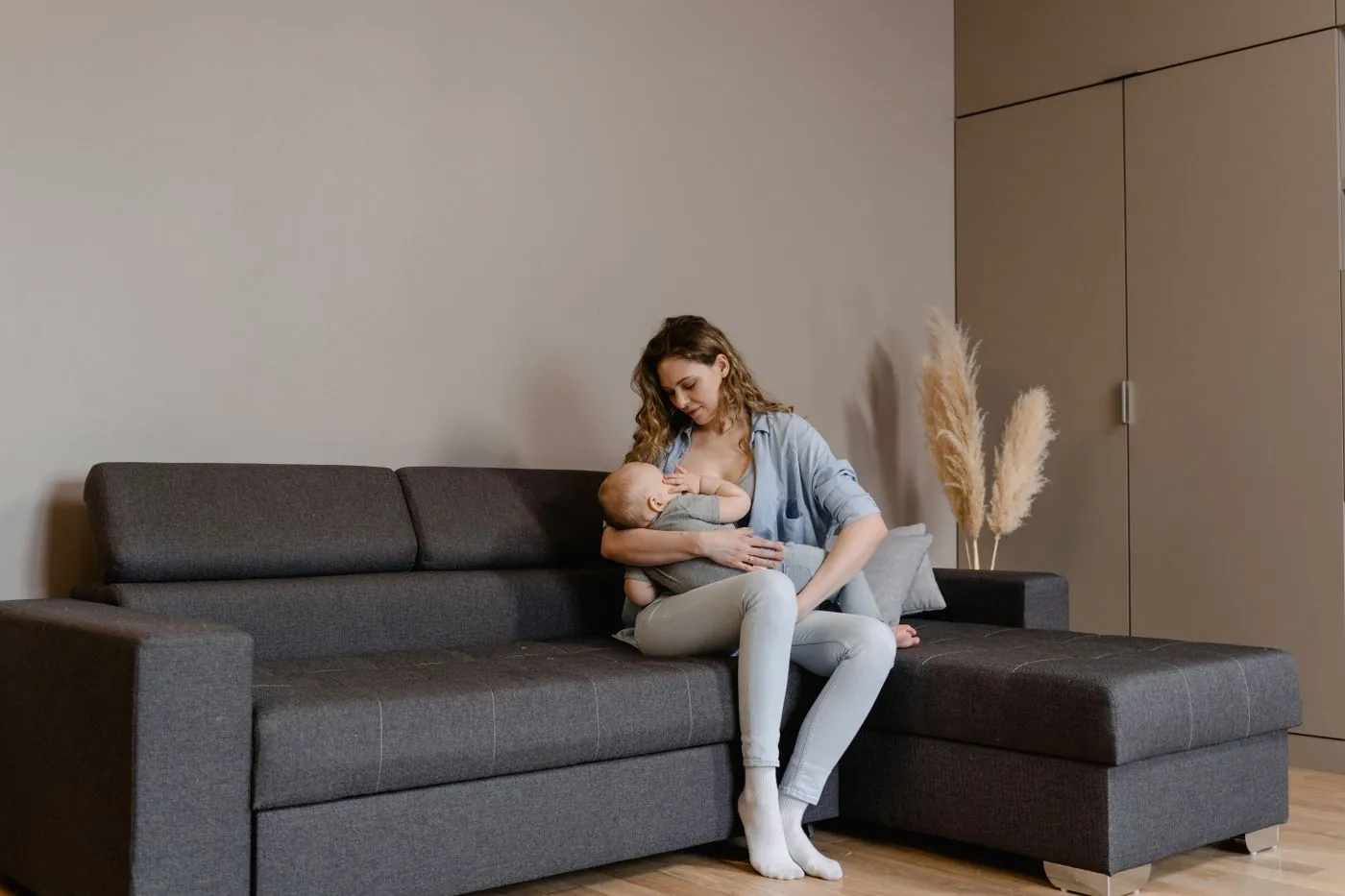 Žena v ležérním oblečení kojí dítě na gauči