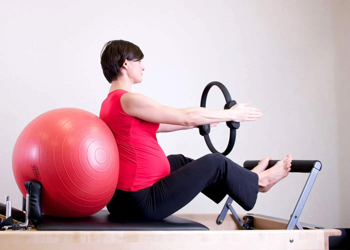 Těhotná žena v červeném topu cvičí pilates s gymballem