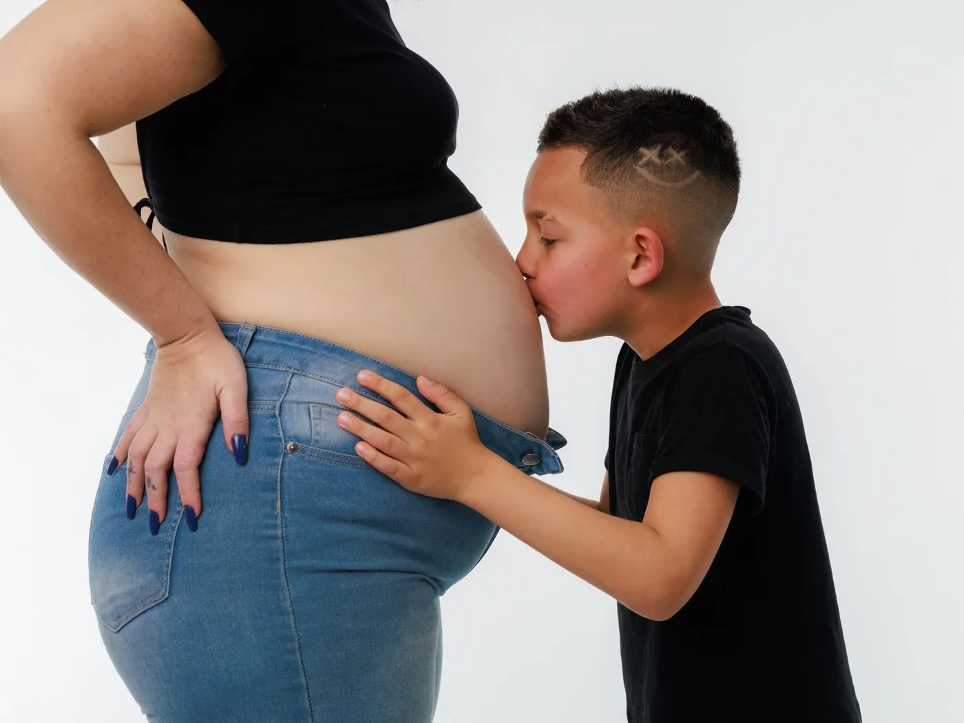 Chlapec líbá bříško těhotné maminky v riflích s nízkým pasem