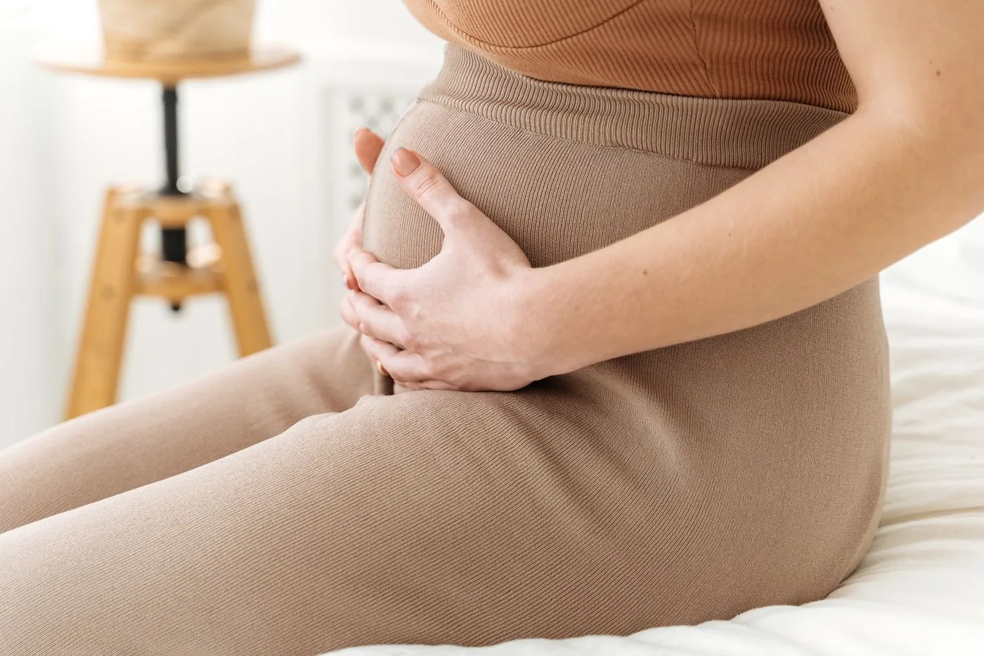 Těhotná žena v béžové sadě spodního prádla sedí na posteli