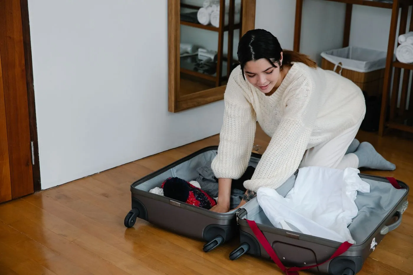 Žena balí oblečení do otevřeného kufru na podlaze